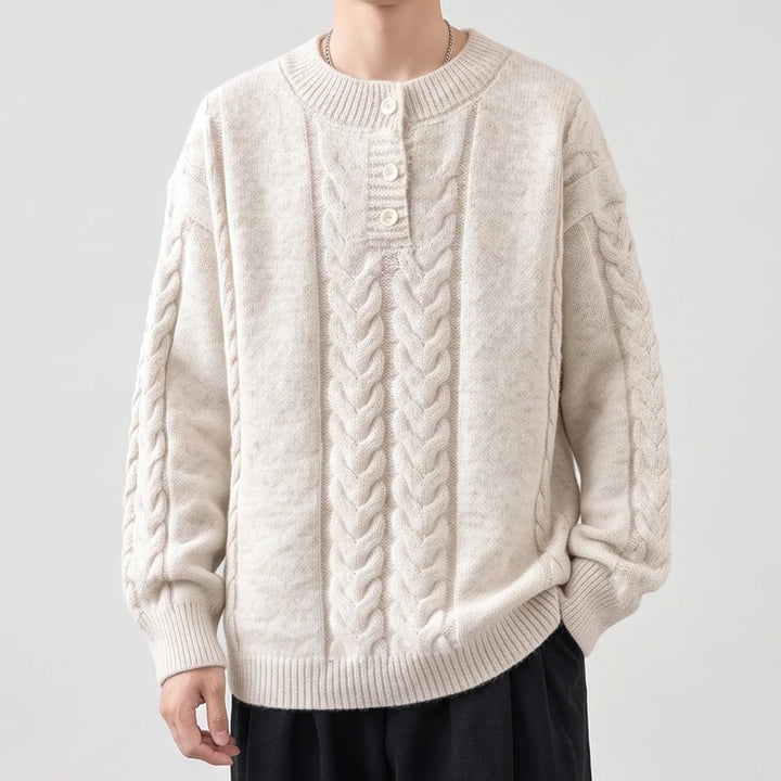 Man wearing a cream cable-knit sweater with a buttoned placket neckline and ribbed cuffs and hem, against a light background.