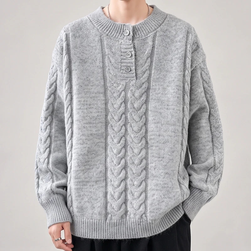 Man wearing a light gray cable-knit sweater with a crew neck and three-button placket, against a plain background.