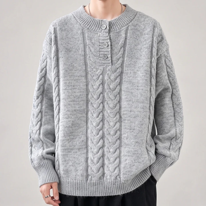 Man wearing a light gray cable-knit sweater with a crew neck and three-button placket, against a plain background.