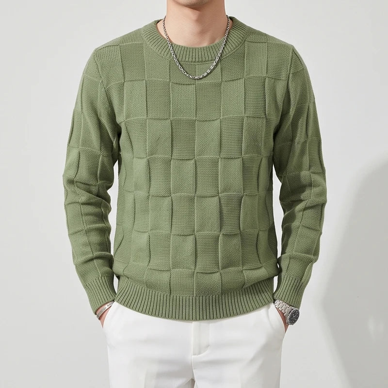 Man wearing a textured olive green knit crew neck sweater with a checkerboard pattern and white pants.
