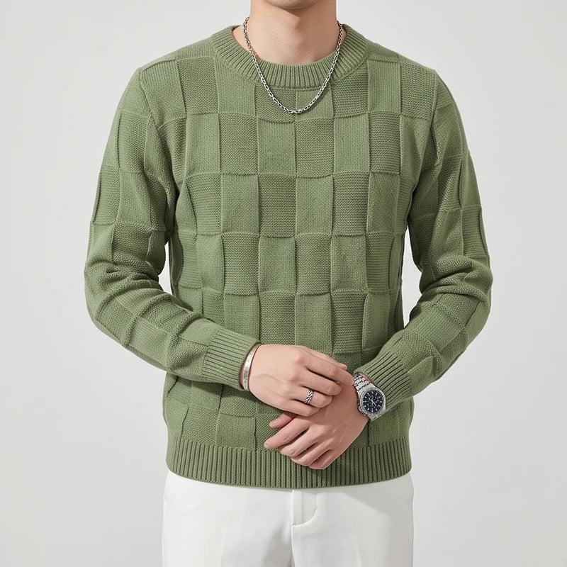 Man wearing a sage green knit sweater with a raised checkered pattern, silver chain, and watch.