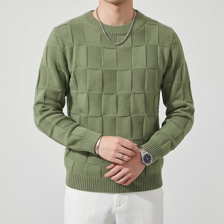 Man wearing a sage green knit sweater with a raised checkered pattern, silver chain, and watch.