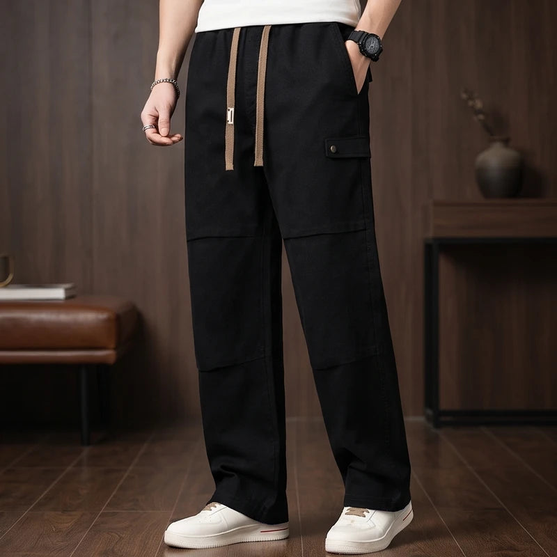 Man wearing black wide-leg cargo pants with a brown drawstring, white sneakers, and a watch, standing indoors.