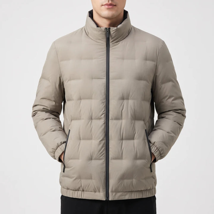 Man wearing a light gray puffer jacket with square quilting, black zipper, and stand-up collar against a white background.