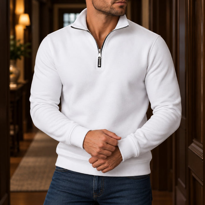 Man wearing a white quarter-zip fleece sweatshirt with a black zipper, paired with blue jeans in a hallway.