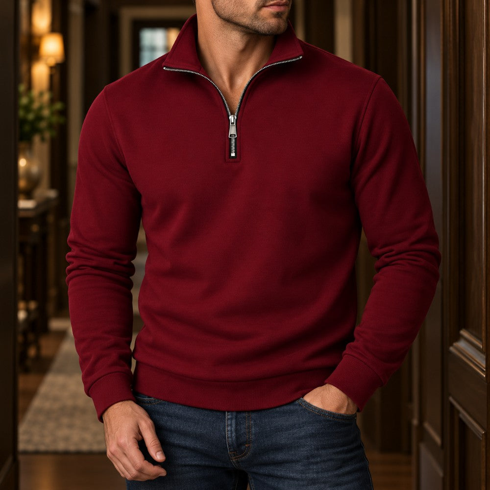 Man wearing a deep red quarter-zip sweatshirt with a silver zipper, blue jeans, standing in a well-lit hallway.