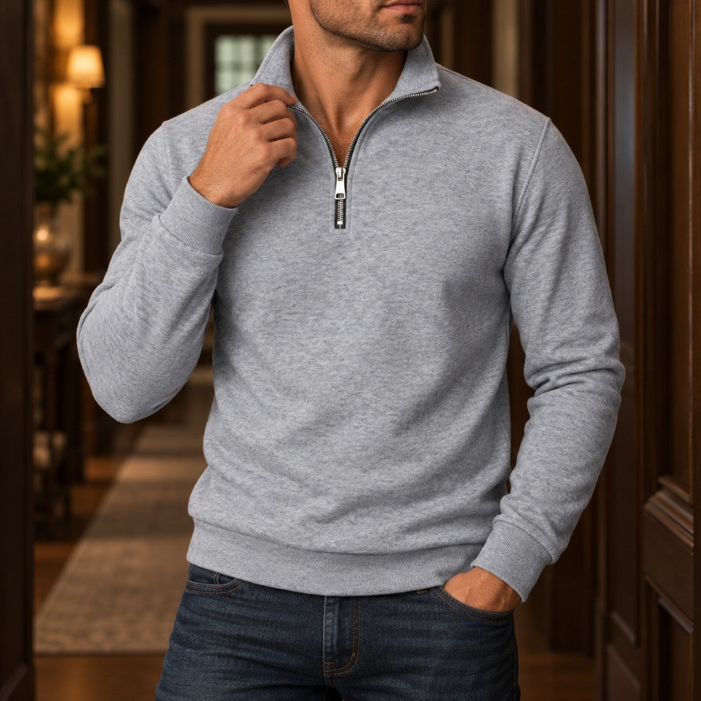Man wearing a light grey quarter-zip fleece sweatshirt with a silver zipper and dark wash jeans.