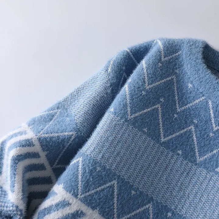 Close-up of a blue knit sweater with white geometric patterns, including zigzags, diamonds, and stripes.