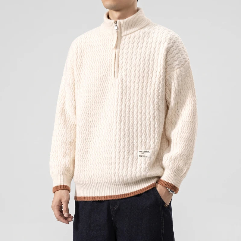 Man wearing a cream half-zip sweater with a wavy knit pattern and brown ribbed cuffs over dark blue pants.