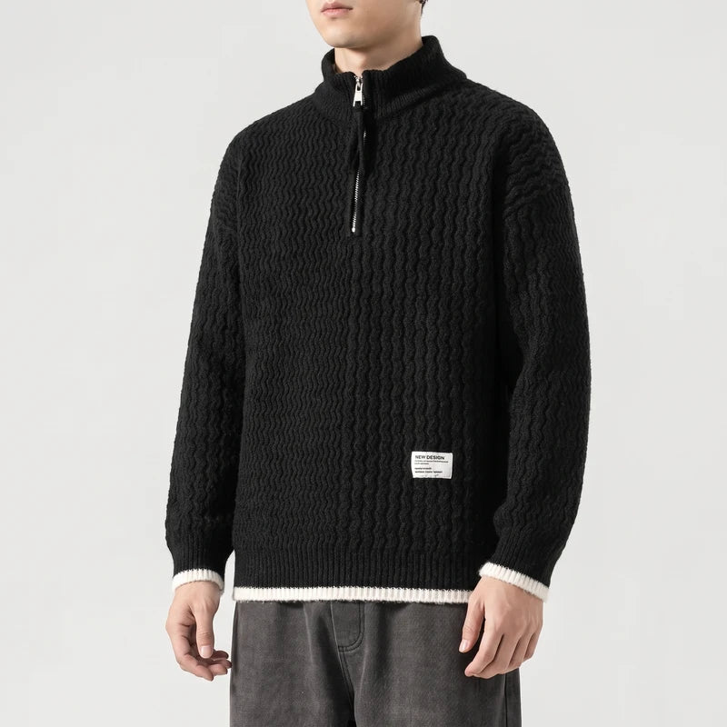 Man wearing a black textured knit sweater with a silver half-zip collar and white ribbed cuffs and hem.
