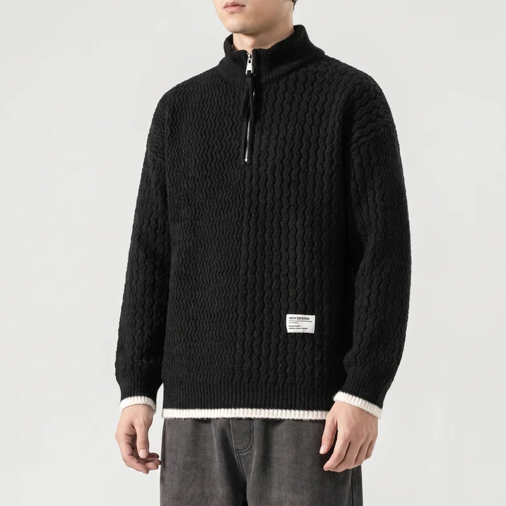 Man wearing a black textured knit sweater with a silver half-zip collar and white ribbed cuffs and hem.