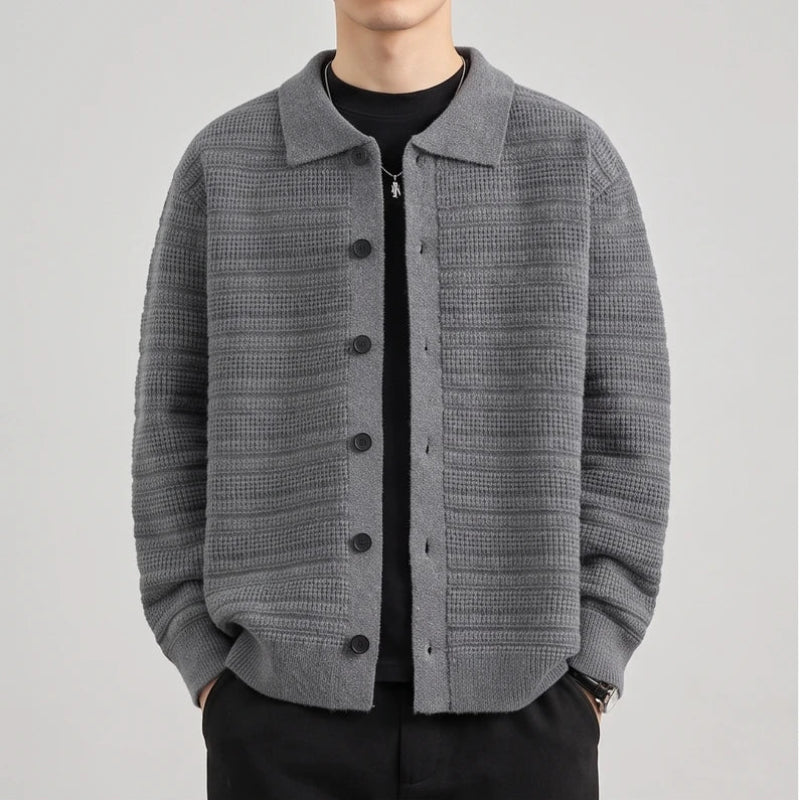 Man wearing a grey knit button-front cardigan with a textured horizontal striped pattern over a black t-shirt.