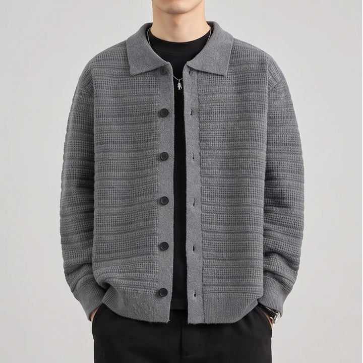 Man wearing a grey knit button-front cardigan with a textured horizontal striped pattern over a black t-shirt.