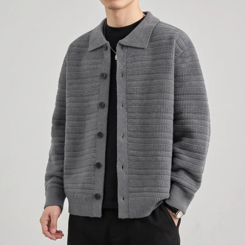 Man wearing an open gray knit cardigan with a shirt collar, textured pattern, and dark buttons over a black t-shirt.