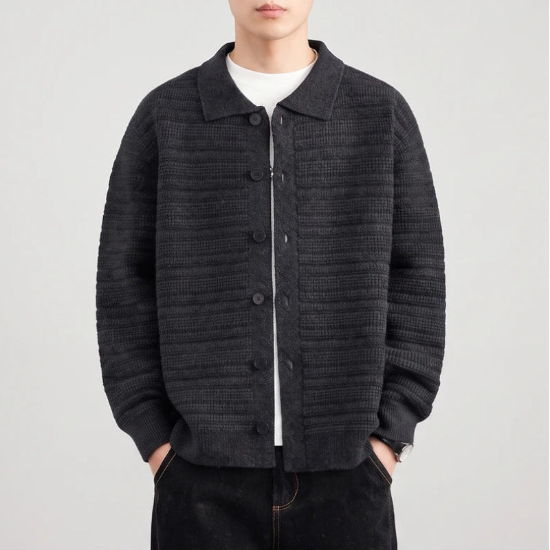Man wearing a dark gray knit button-front cardigan with a collar over a white shirt, hands in pockets.