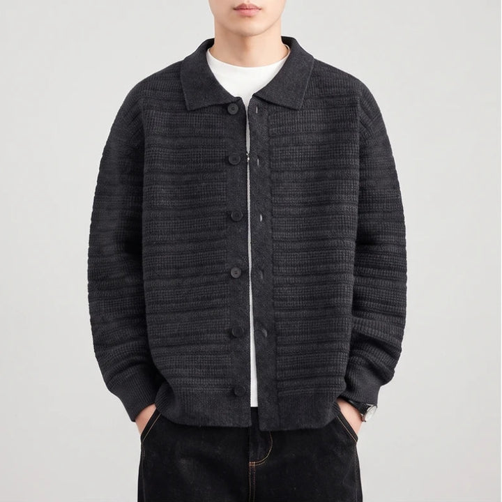 Man wearing a dark gray knit button-front cardigan with a collar over a white shirt, hands in pockets.
