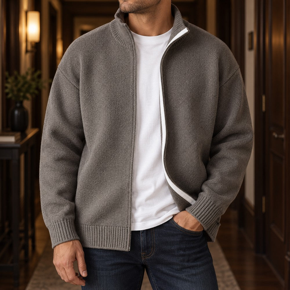 Man wearing an open gray knit cardigan sweater over a white t-shirt, with one hand in his jeans pocket.