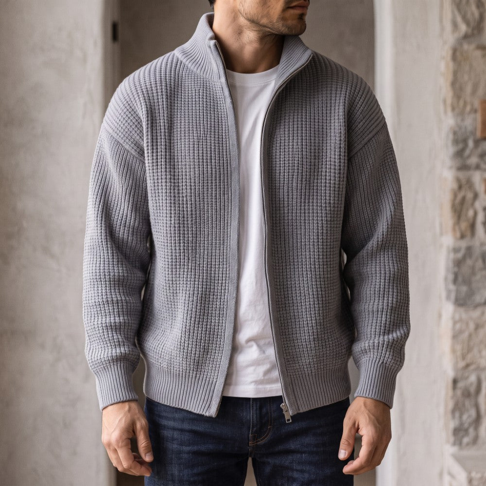 Man wearing an open light gray waffle knit zip-up cardigan over a white t-shirt and blue jeans.