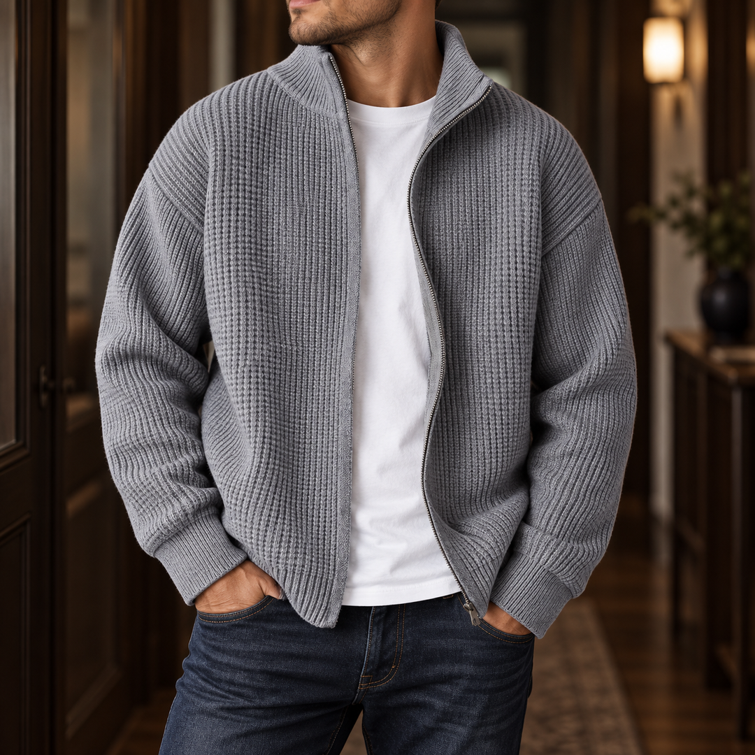 Man wearing an open gray waffle knit cardigan with a full zipper, a white t-shirt, and dark blue jeans.