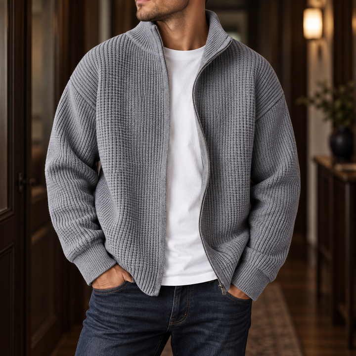 Man wearing an open gray waffle knit cardigan with a full zipper, a white t-shirt, and dark blue jeans.