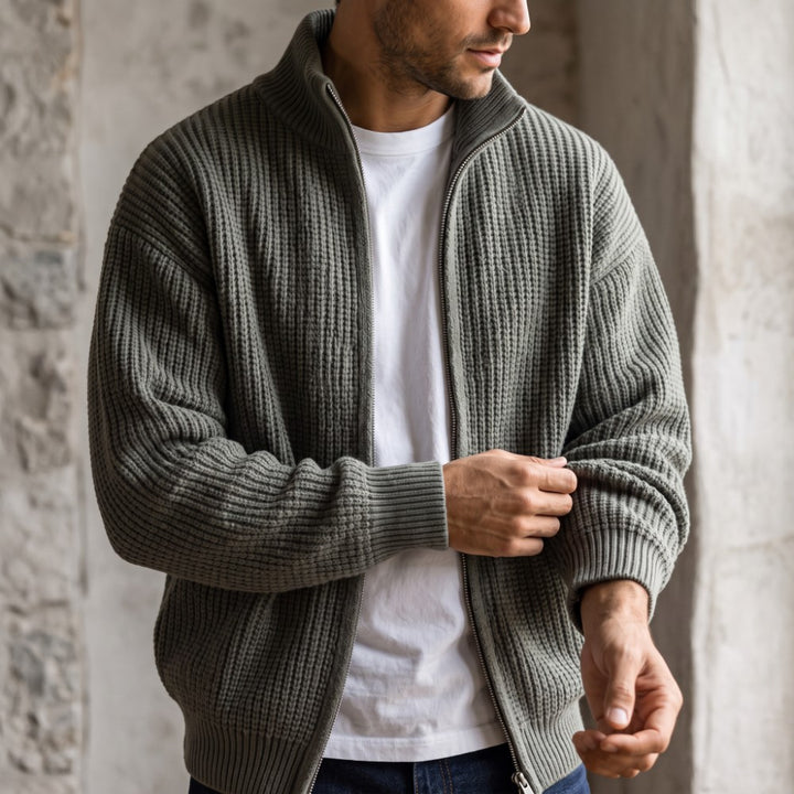 Man wearing an open gray-green waffle knit cardigan over a white t-shirt, adjusting the sleeve cuff.