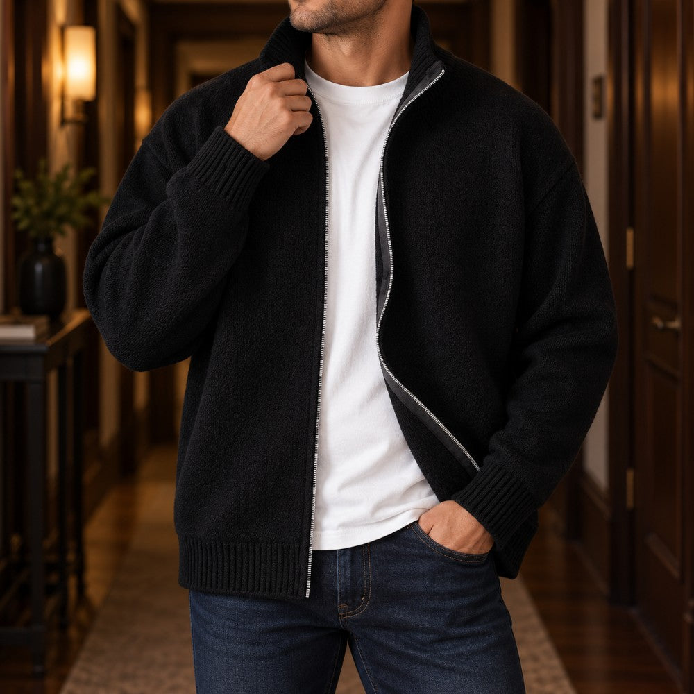 Man wearing a partially unzipped black knit cardigan with a ribbed collar, cuffs, and hem, over a white t-shirt.