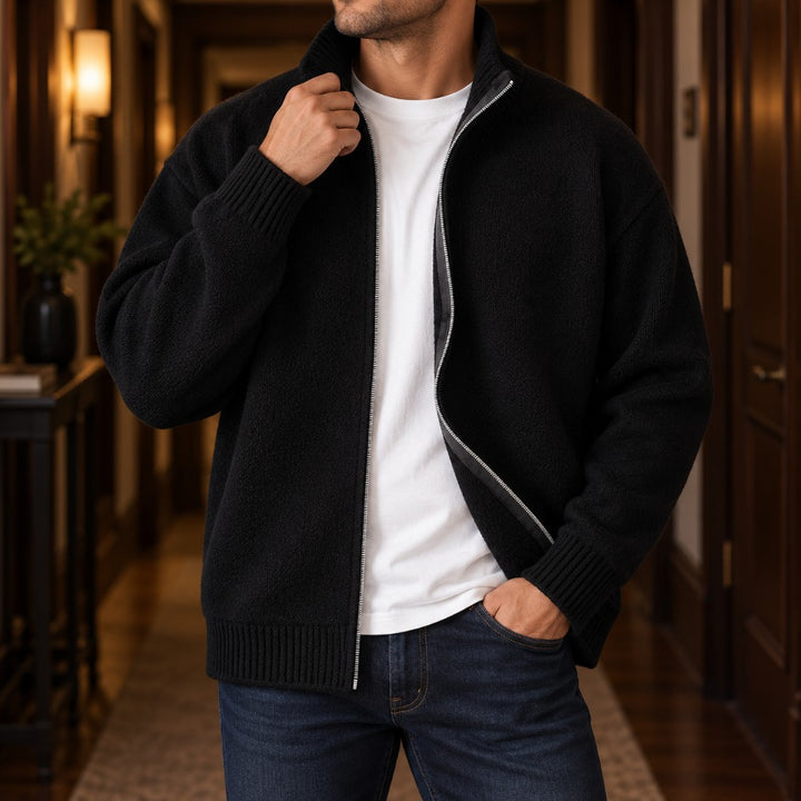 Man wearing a partially unzipped black knit cardigan with a ribbed collar, cuffs, and hem, over a white t-shirt.