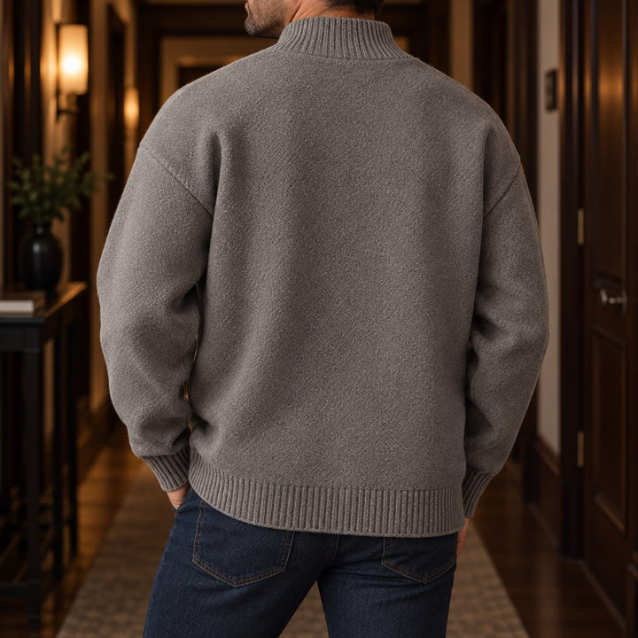 Man wearing a textured gray knit cardigan sweater and dark blue jeans, viewed from the back in a hallway.