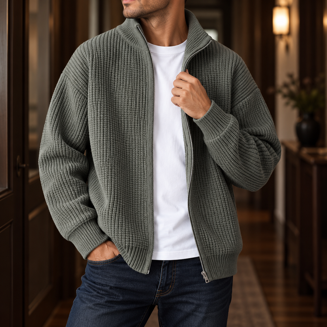 Man wearing an unzipped sage green textured knit cardigan over a white t-shirt, hand in jeans pocket.
