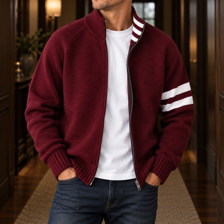 Man wearing an open, dark red knit cardigan with white stripes on the arm and collar, over a white t-shirt and jeans.