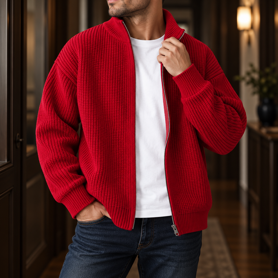 Man wearing an open, textured red knit cardigan over a white t-shirt and blue jeans in a hallway.