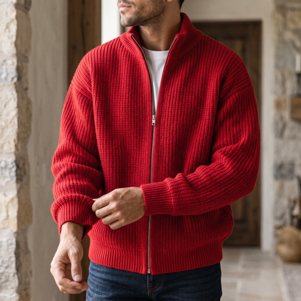 Man adjusting the cuff of a chunky red knit cardigan with a silver zipper, worn over a white shirt and blue jeans.