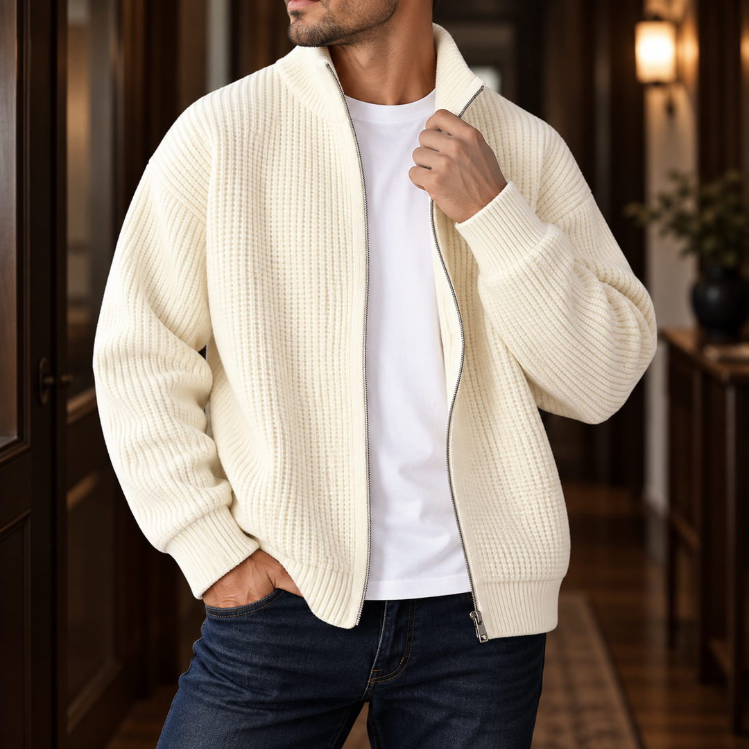 Man wearing a cream ribbed knit cardigan with a silver zipper over a white t-shirt and dark blue jeans.