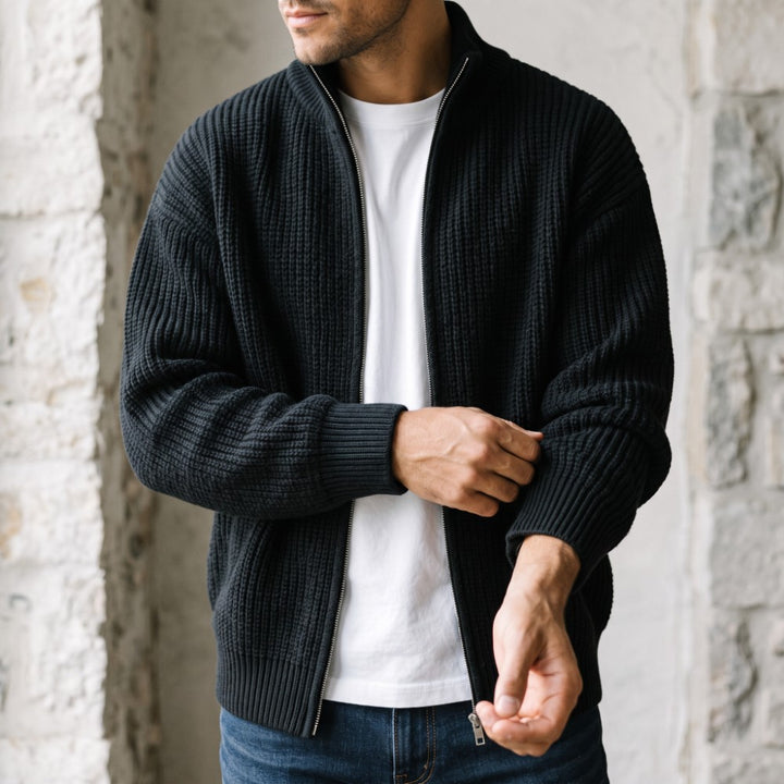 Man wearing a black ribbed knit full-zip cardigan over a white t-shirt, adjusting the cuff.