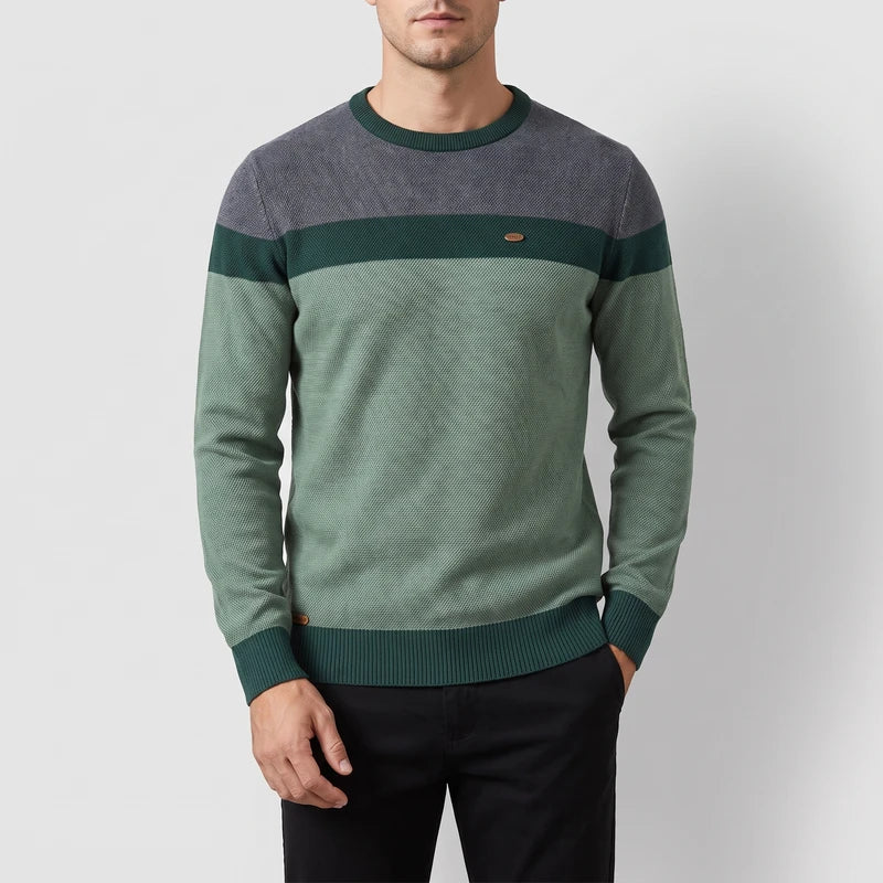 Man wearing a crew neck sweater with grey, dark green, and light green color blocks, featuring a textured knit.