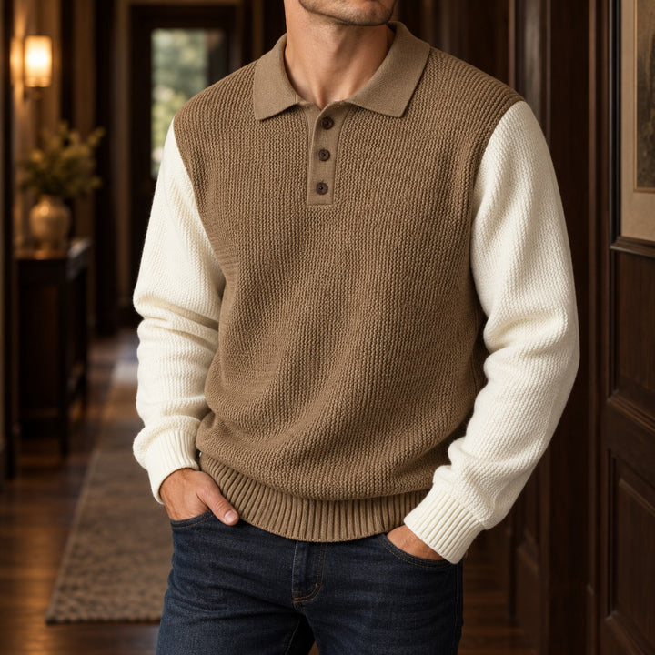 Man wearing a two-tone knit polo sweater, with a textured brown body, cream sleeves, and three brown buttons, standing in a hallway.