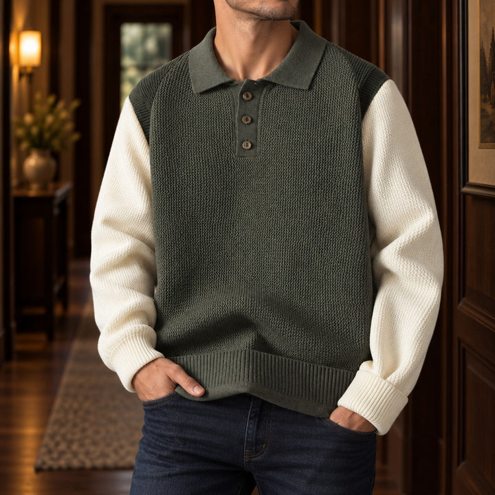 Man wearing a two-toned knit polo sweater with dark green body and cream sleeves, hands in dark blue jeans pockets.
