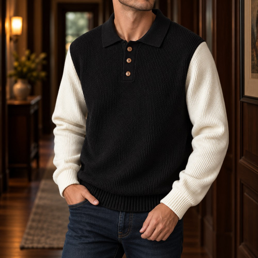 Man wearing a black and white color-block knit polo sweater with wooden buttons and dark jeans, hands in pockets.