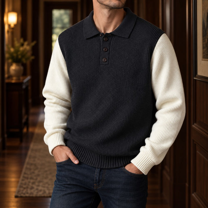 Man wearing a color-block knit polo sweater with a dark gray body and off-white sleeves, posing with hands in pockets.