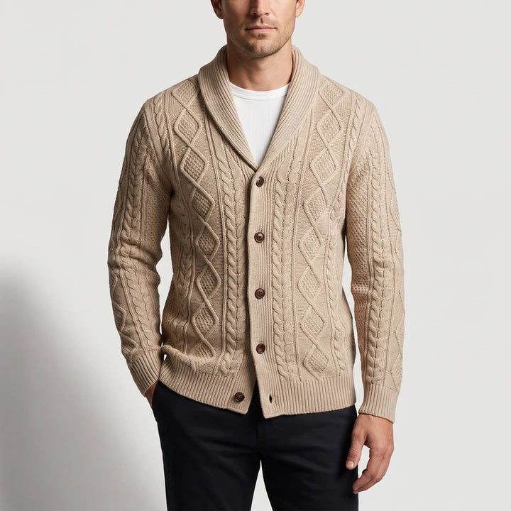 Man wearing a light tan cable knit cardigan with a large shawl collar and brown buttons, over a white t-shirt.