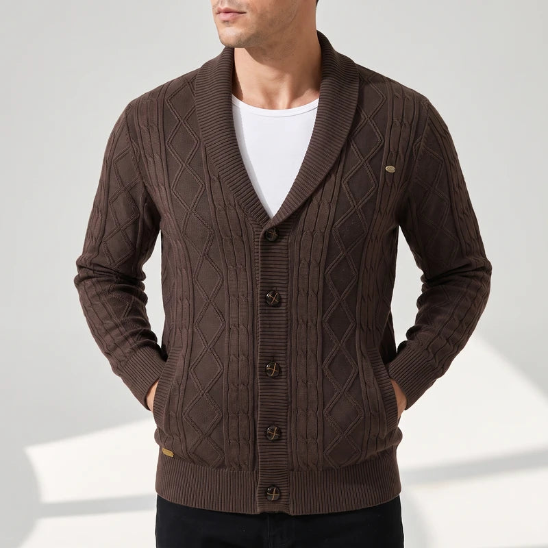 Man wearing a brown cable knit cardigan with a shawl collar, button-front closure, and side pockets against a white background.