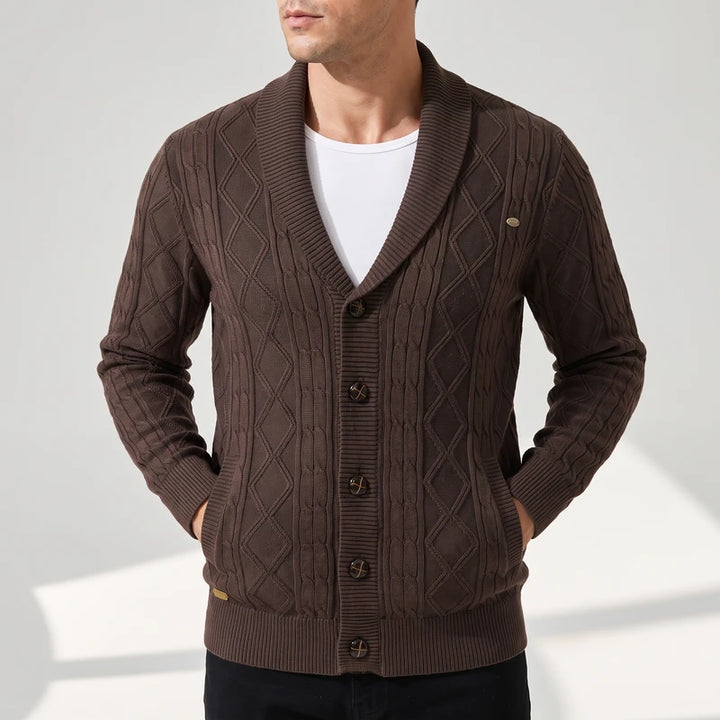 Man wearing a brown cable knit cardigan with a shawl collar, button-front closure, and side pockets against a white background.