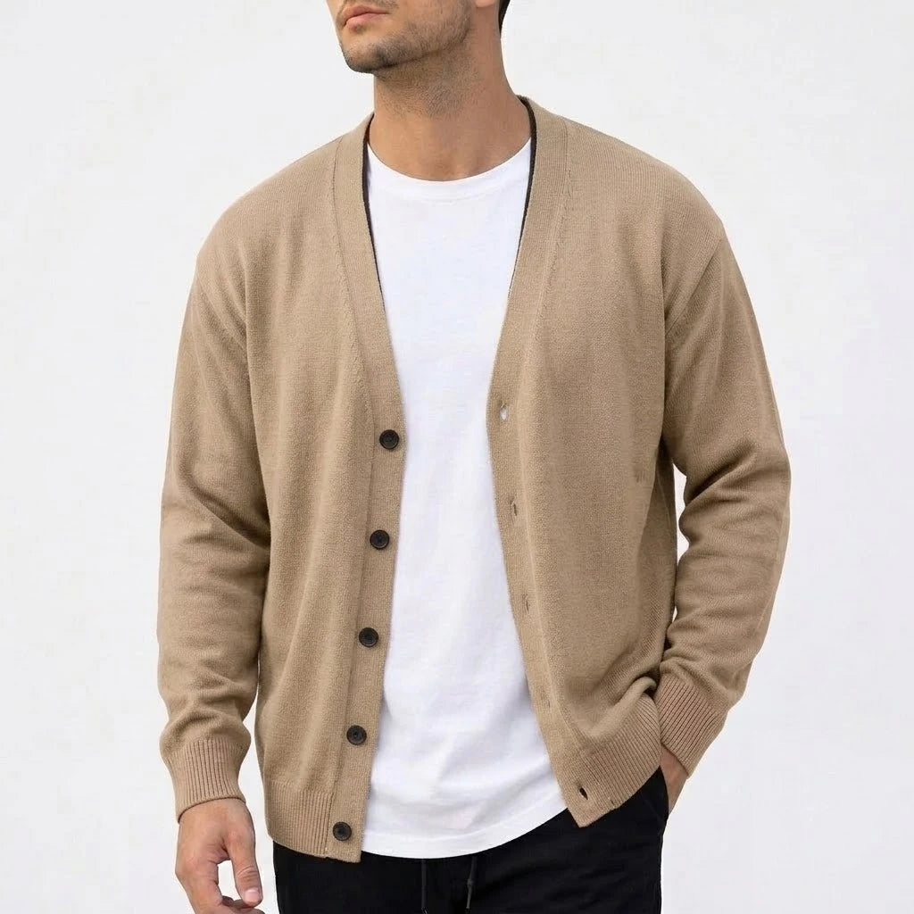Man wearing a relaxed-fit tan knit cardigan with dark brown buttons over a white t-shirt, standing against a white background.