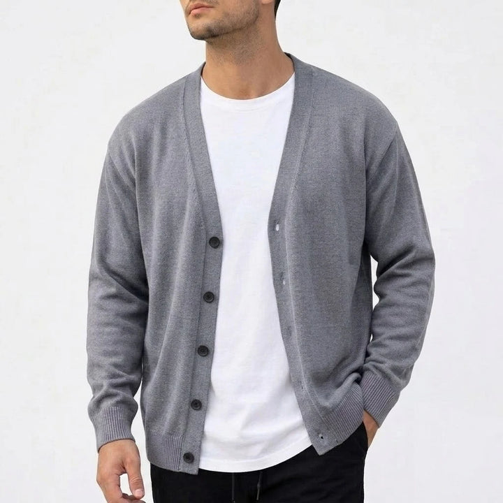 Man wearing a loose-fit, light grey knit V-neck cardigan over a white t-shirt, with dark buttons visible.