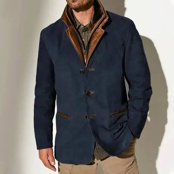 Man wearing a dark blue three-button jacket with a brown leather collar and pocket trim over a gray shirt.