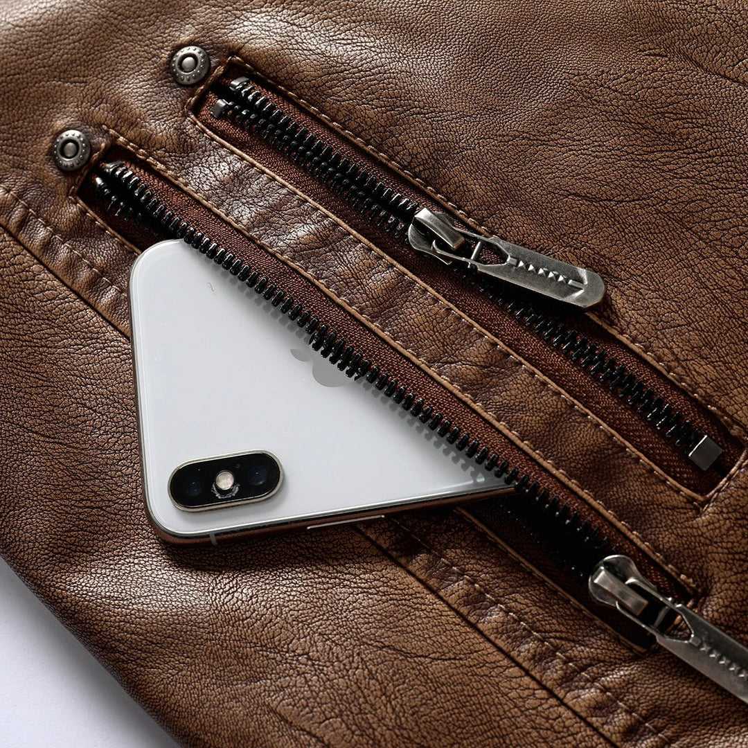 Close-up of a brown textured leather jacket pocket with a white smartphone tucked inside, showing metal zippers and snaps.