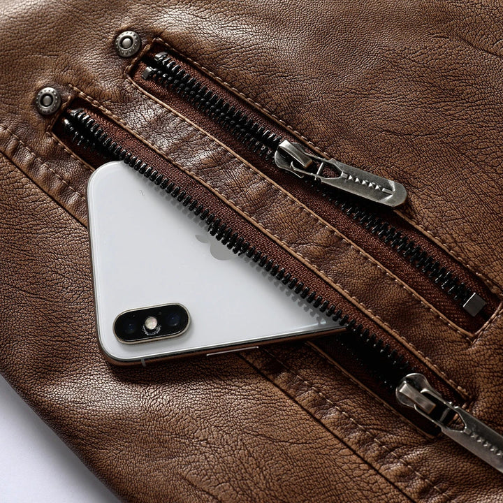 Close-up of a brown textured leather jacket pocket with a white smartphone tucked inside, showing metal zippers and snaps.