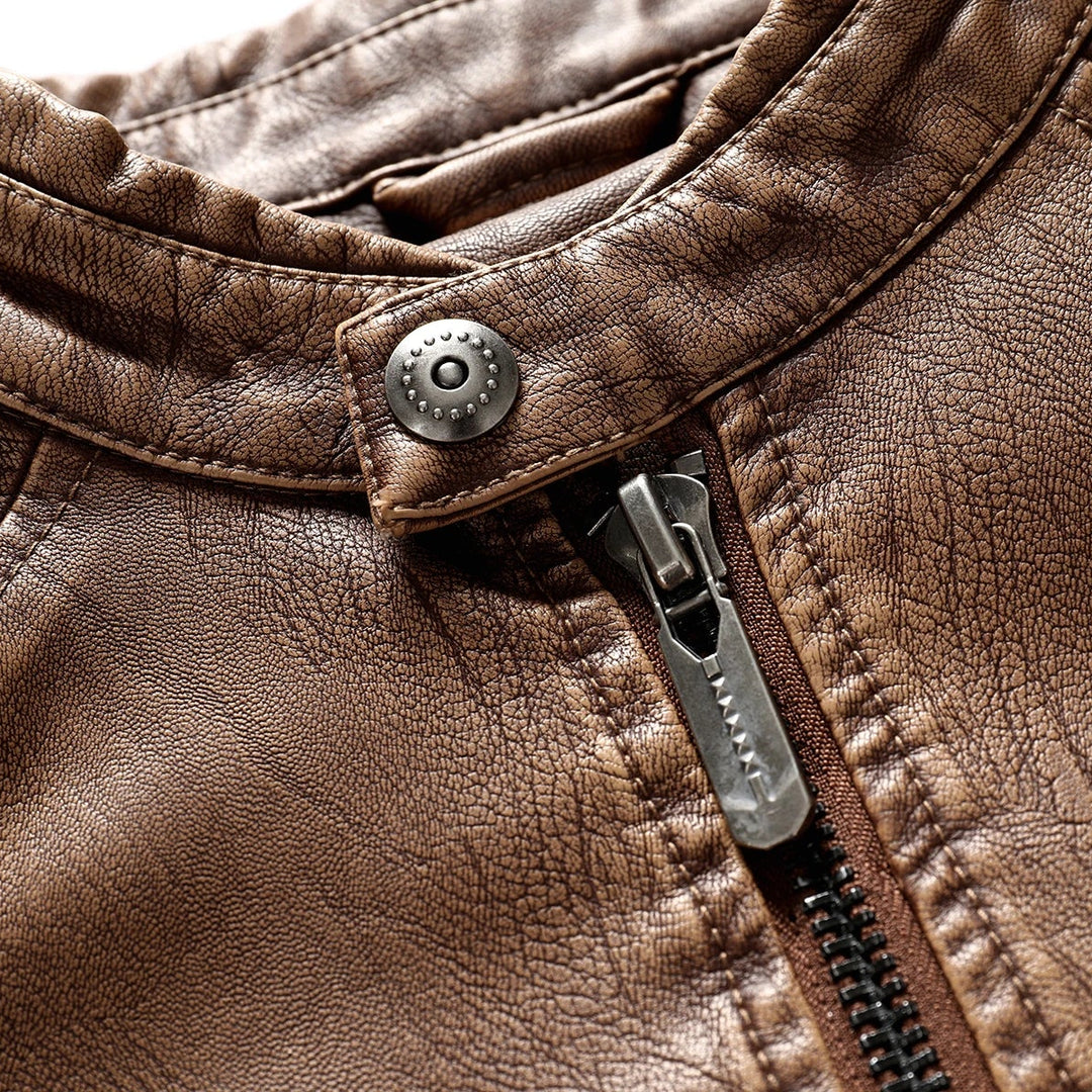 Close-up of a textured brown leather jacket collar with an antique silver snap button and a dark metal zipper.