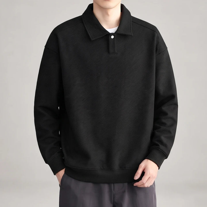 Man wearing a black long-sleeve polo sweatshirt with a textured diagonal stripe pattern and white buttons, hands in pockets.