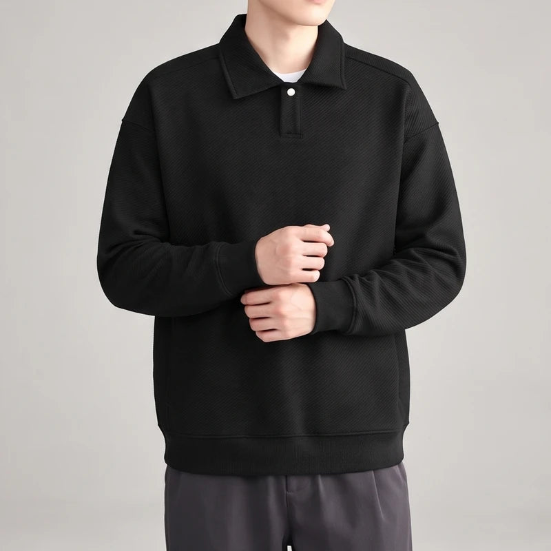 Man wearing a black long-sleeve polo sweatshirt with a textured diagonal stripe pattern, white button, and ribbed cuffs.